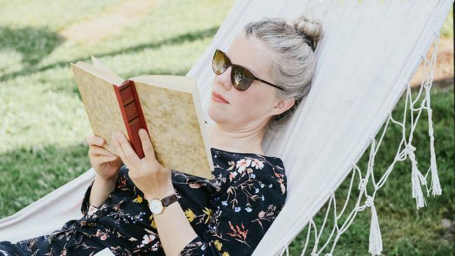 Summer woman lies in a white hammock reading a book.