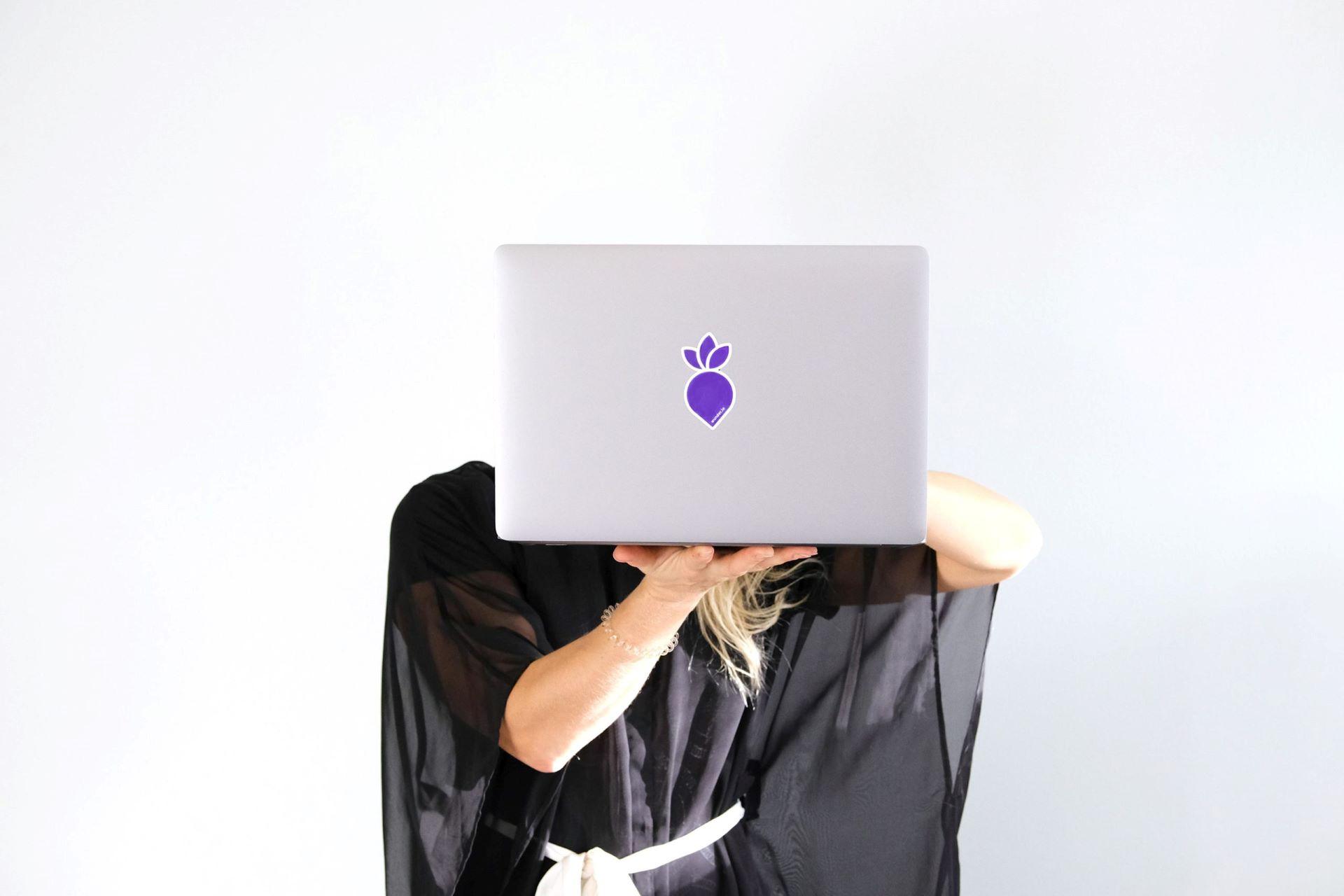 A woman with a laptop in her hand helding it in front of her face